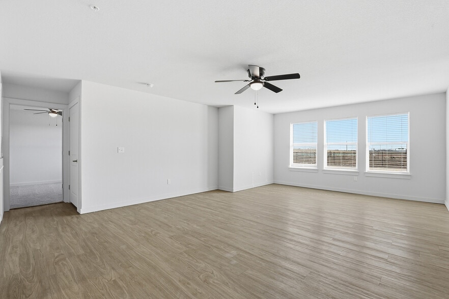 Bright and spacious living room with sleek wood flooring, large windows offering natural light, and a modern ceiling fan. - Oaks at Mustang