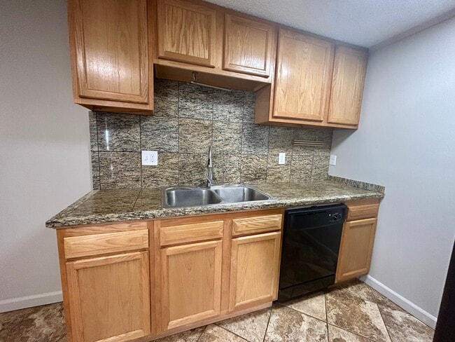 Modern kitchen with sleek granite countertops, wooden cabinets, and black appliances in a stylish apartment setting. - Boardwalk Apartments
