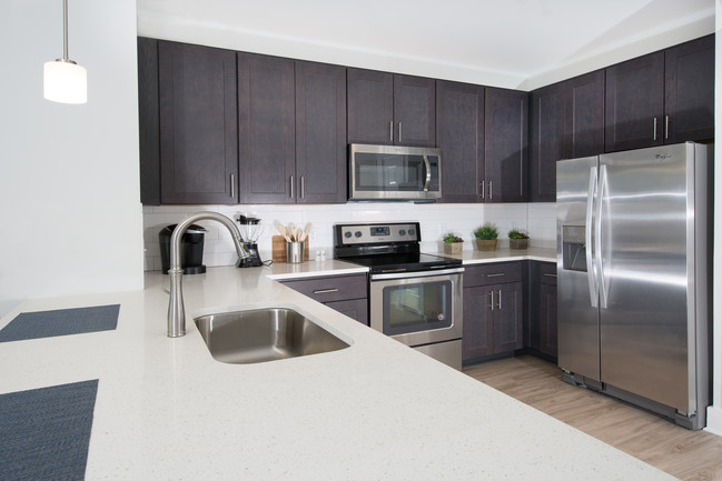 Gorgeous kitchen with shaker style cabinets, side by side stainless refrigerator, quartz countertops farmhouse sink and pendant lighting - The Haven at Indigo Square