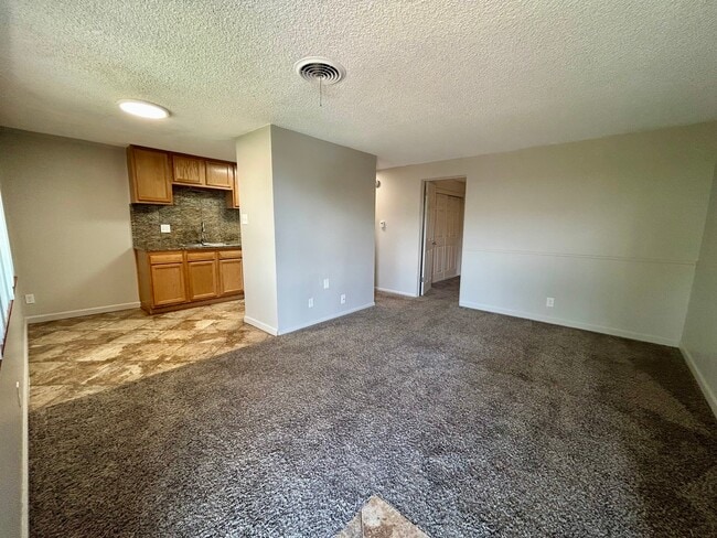 Inviting op en-concept living space with plush carpet, adjoining a cozy kitchen with wood cabinets and stylish tile flooring. - Boardwalk Apartments
