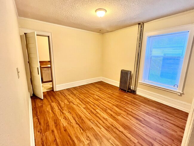 Experience the comfort of this cozy bedroom, featuring elegant hardwood flooring and ample natural light. - Cross Apartments
