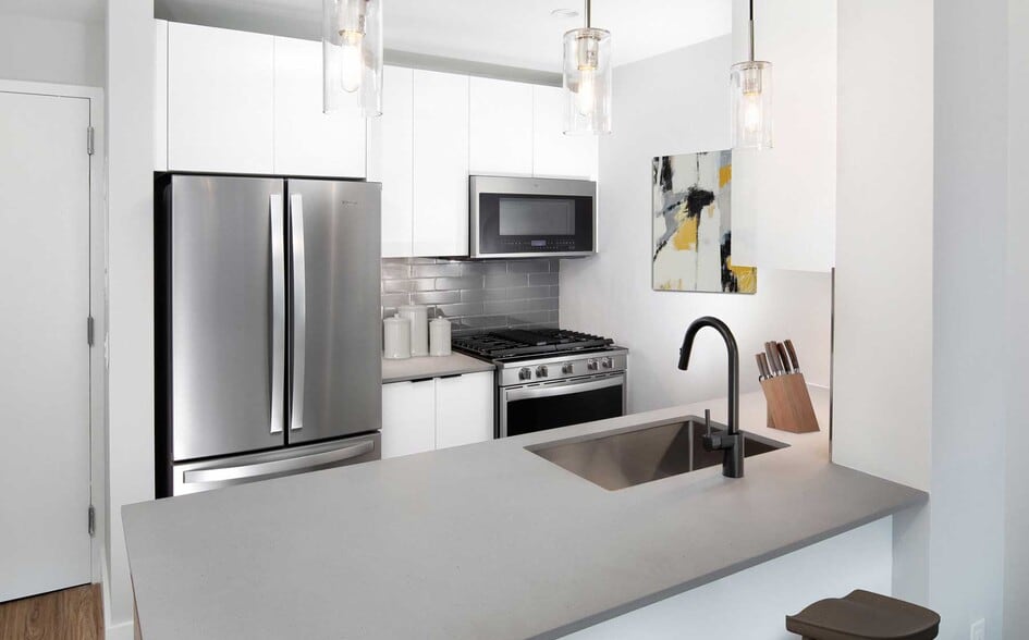 Renovated Package I kitchen with stainless steel appliances, white cabinetry, grey tile backsplash, grey quartz countertops, and hard-surface flooring (Representative Imagery) - Avalon Riverview