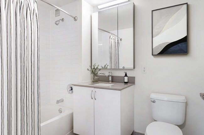 Updated Finishes bath with white cabinetry, grey quartz countertops, and hard surface flooring - AVA Fort Greene