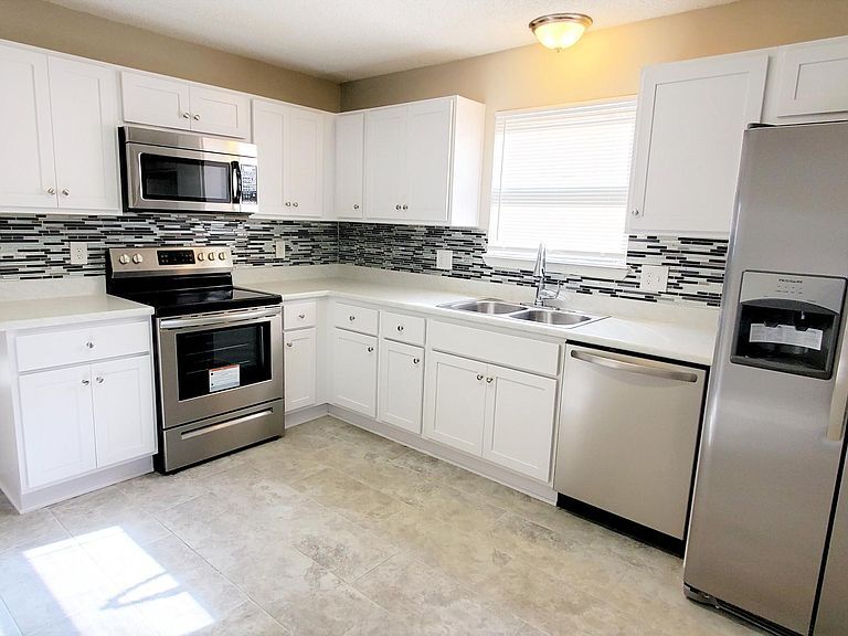 Open layout kitchen with new tile backsplash, new white shaker cabinets, and brand new stainless steel appliances including: side by side refrigerator, energy efficient dishwasher, electric range/oven, and over the range vented microwave. - 1300 Bay Hill Blvd.