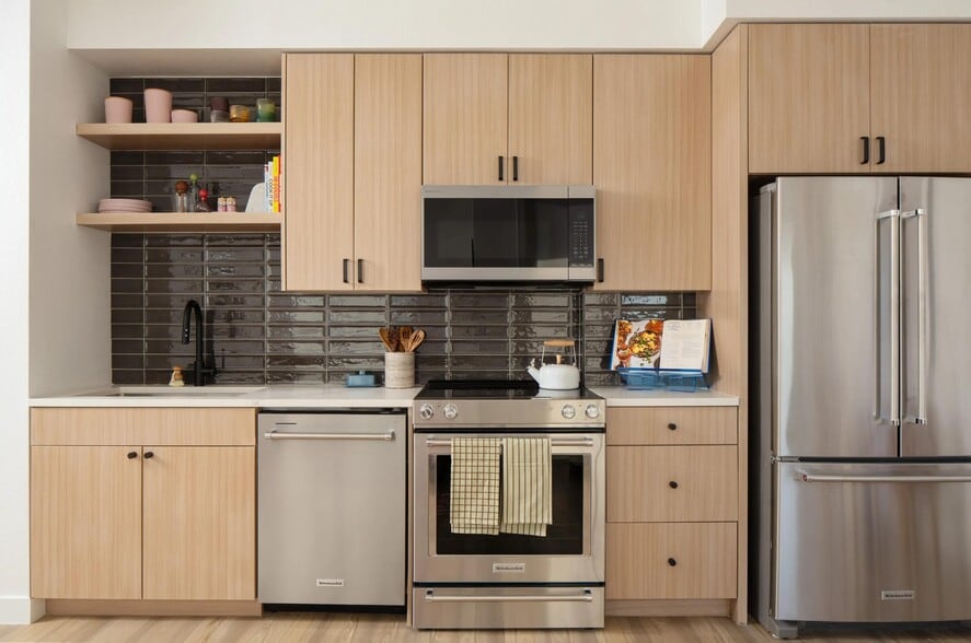 Light wood cabinetry, sleek stainless appliances, and a glossy tile backsplash create a clean, contemporary kitchen with character. - Modera Rio Salado
