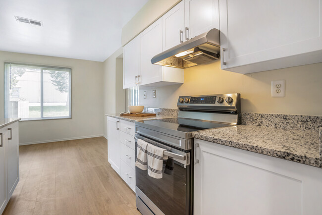 Renovated Package II kitchen featuring stainless steel appliances, white cabinetry, white speckled granite countertops, and hard surface flooring - eaves Tysons Corner