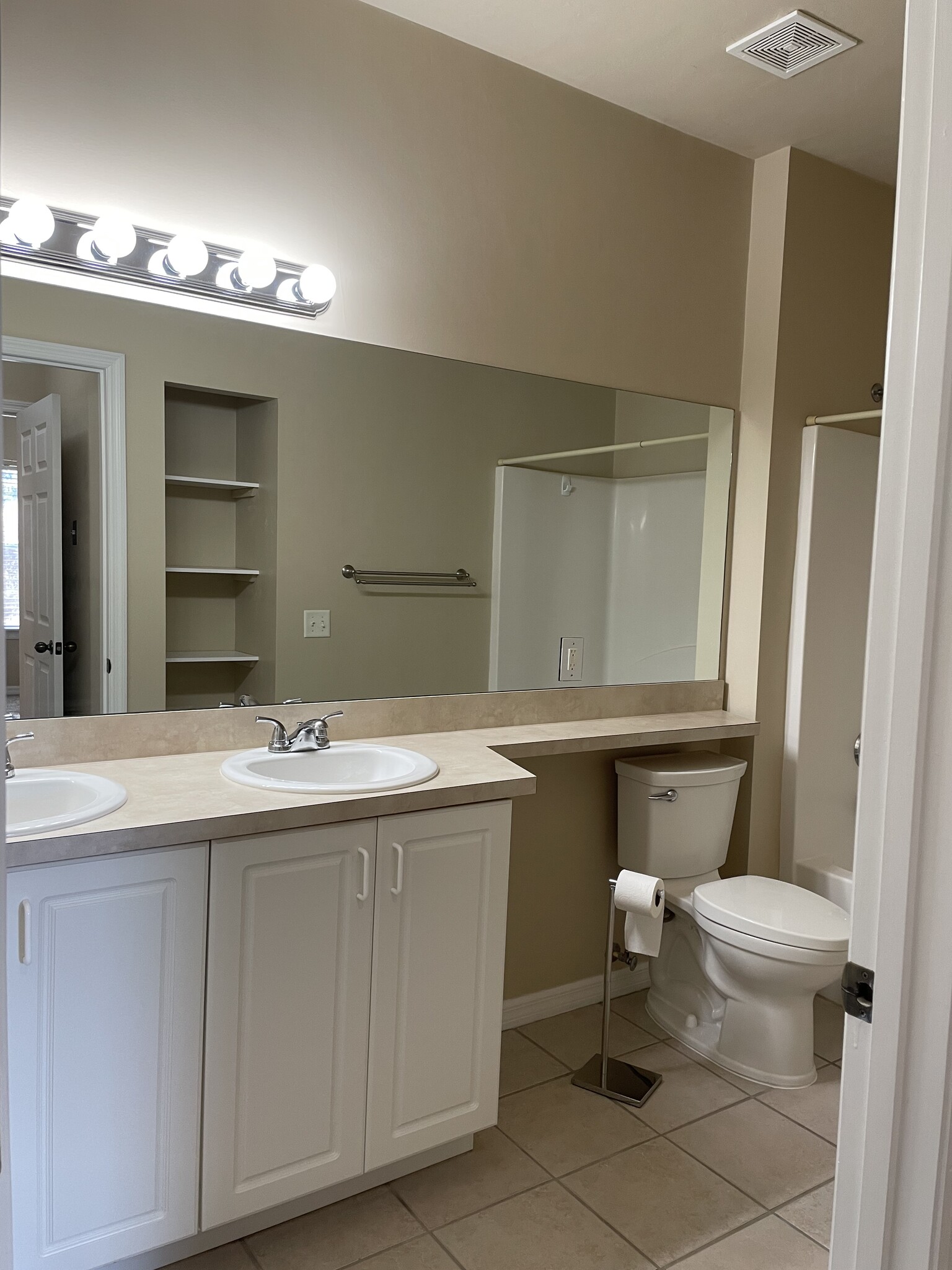 An elongated mirror above dual sinks and cabinet across from linen and towel shelves. - 13200 W Newberry Rd