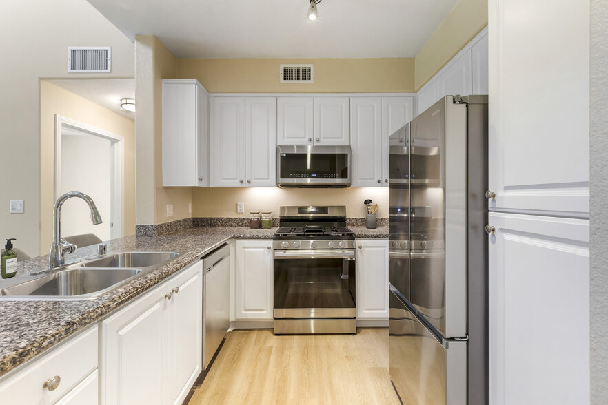 Renovated Package I kitchen with stainless steel appliances, beige speckled granite countertop, white cabinetry, and hard surface flooring - Avalon Glendale