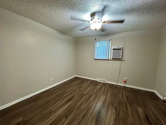 Inviting room with modern wood flooring, neutral walls, a bright ceiling fan, and efficient window AC unit. - Boardwalk Apartments