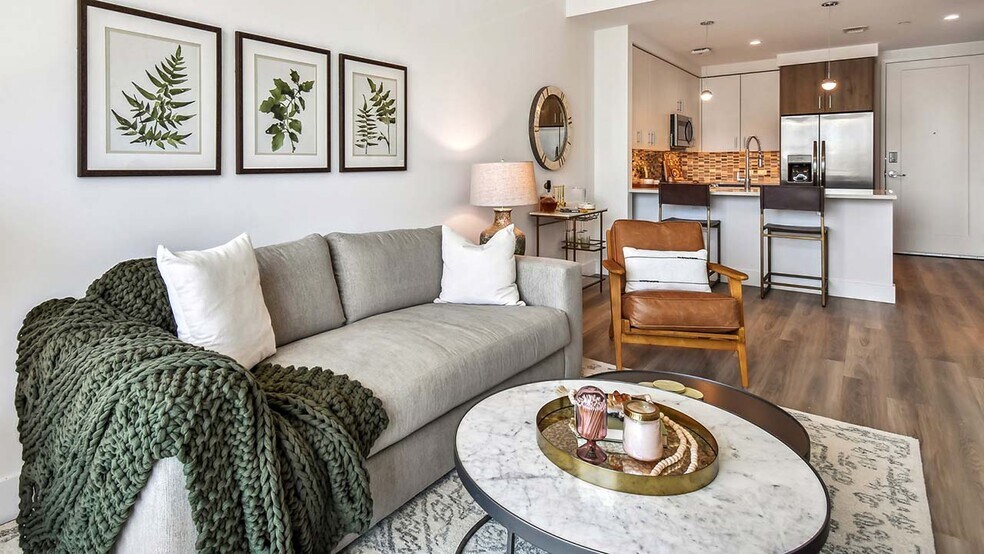 Griffis West Palm apartment living room with pattern rug, plush couch, framed artwork, and round tables. - Griffis West Palm