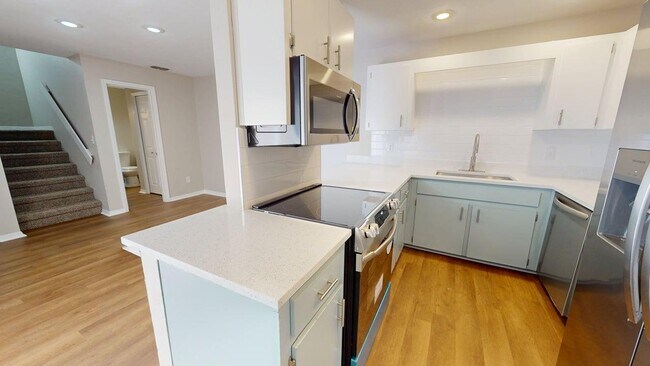 Modern kitchen with sleek stainless steel appliances, elegant cabinetry, and gleaming wooden floors, adjacent to a cozy carpeted stairway. - Villas of Stone Ridge