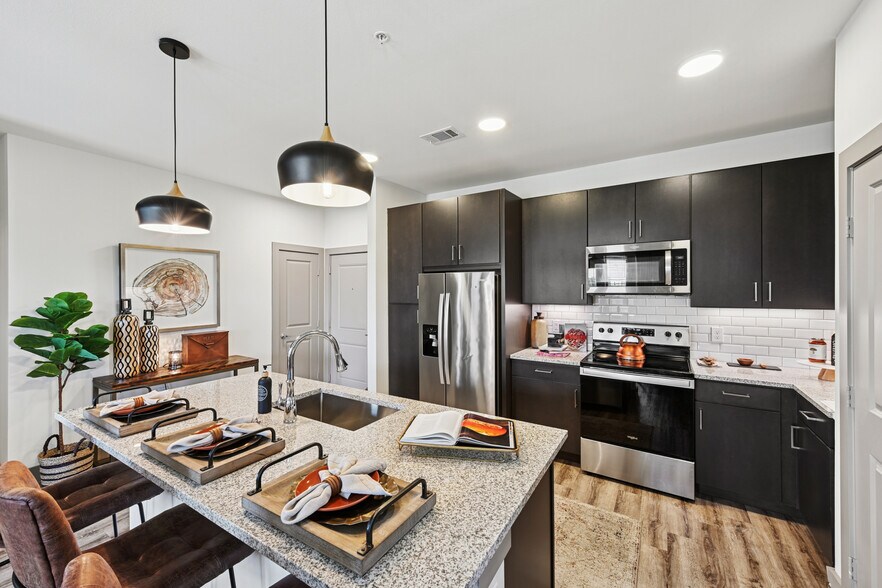 Kitchen with espresso cabinetry, speckled granite countertops, white subway tile backsplash, stainless steel appliances, and hard surface flooring - Avalon Benbrook
