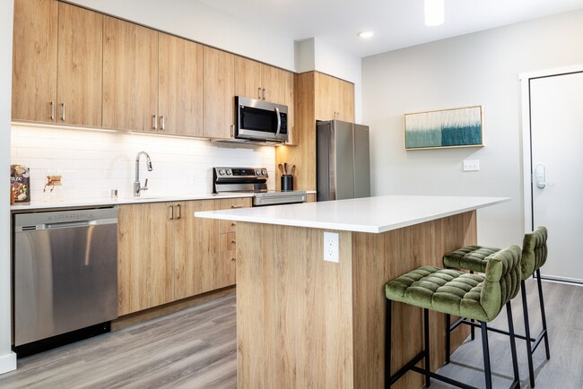 Kitchen with oak cabinetry, white granite countertops, white tile backsplash and stainless steel appliances - Avalon Redmond Campus