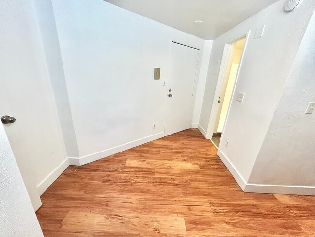 Inviting apartment entryway featuring elegant hardwood floors and sleek white walls, setting a modern tone. - Plaza West