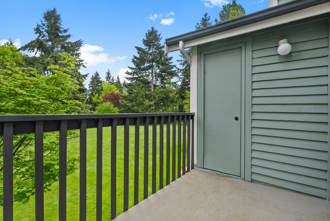 A private balcony offering peaceful views of the surrounding lawn and mature trees, perfect for relaxing outdoors. - Windemere Apartments
