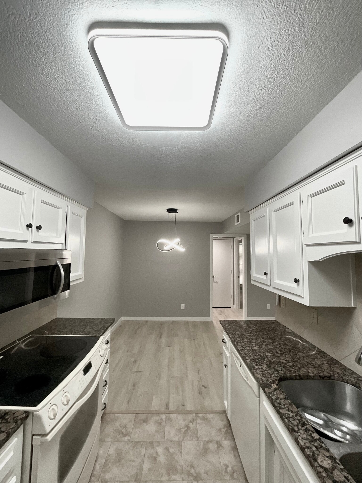 The kitchen features a granite countertop, spacious cabinets, large LED lighting, and a tiled floor. - 12743 W 110th Ter