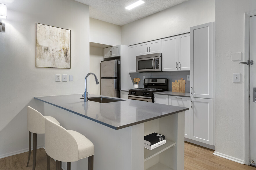 Renovated Package III kitchen with grey quartz countertops, white cabinetry, stainless steel appliances, tile backsplash, and hard surface plank flooring - Avalon Cove