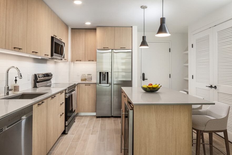 Kitchen with stainless steel appliances, grey quartz countertops, white tile backsplash, and hard surface flooring - Avalon Merrick Park