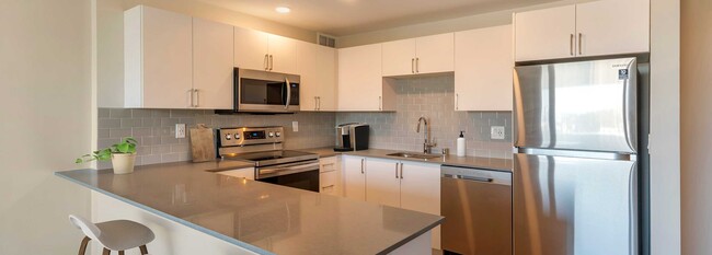 Limited availability: newly renovated Finish Package II apartment homes featuring kitchens with grey quartz countertops, white cabinetry, stainless steel appliances, grey tile backsplash, and hard surface flooring - Avalon Sunset Towers