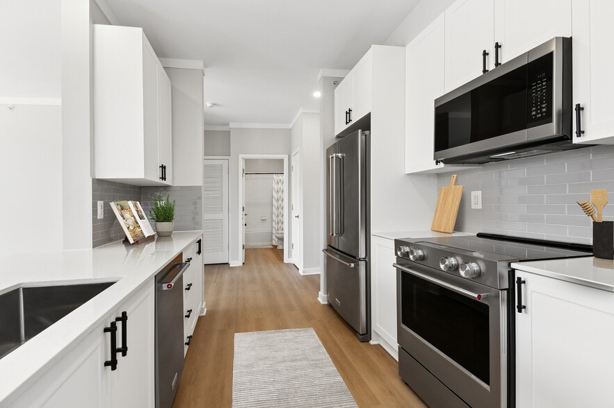 Renovated Package II kitchen with stainless steel appliances, white cabinetry, grey tile backsplash, white quartz countertops, and hard surface flooring - Avalon Falls Church