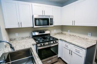 Stainless steel microwave and gas range with white shaker cabinets, granite counter, and large sink. - The Lido Apartments