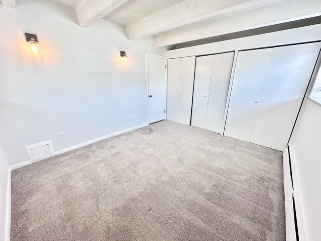 Bright room with plush carpeting featuring modern wall lighting and ample closet space. - Columbine Plaza