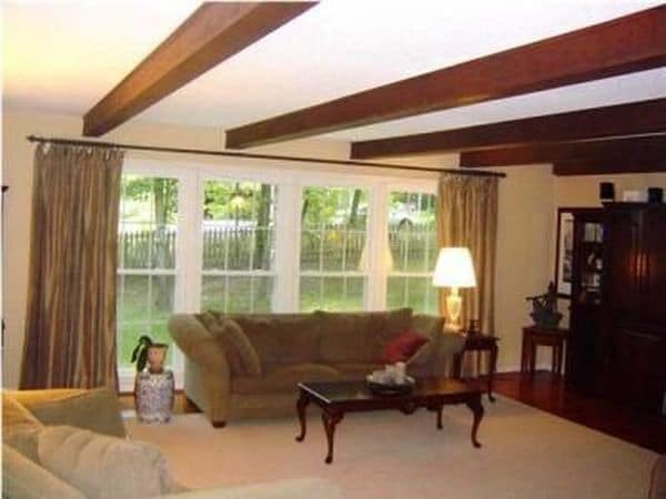 Exposed ceiling beams in main level living room, floor to ceiling windows look into back yard - 303 Ferncliff Dr