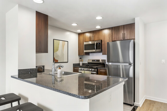 Updated Finishes kitchen with espresso cabinetry, dark speckled granite countertops, white tile backsplash, stainless steel appliances, and hard surface flooring - AVA Fort Greene