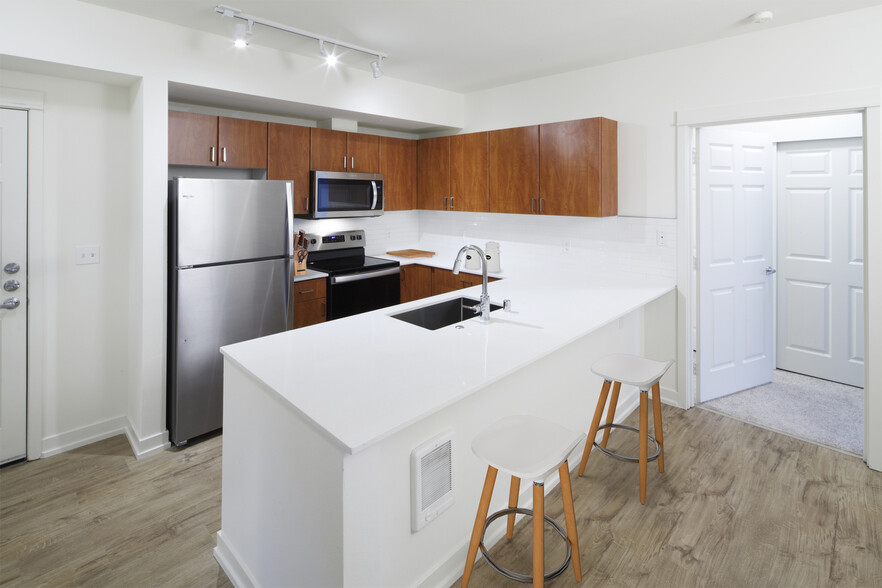 Renovated Package I kitchen with white quartz countertops, oak cabinetry, stainless steel appliances, tile backsplash, and hard surface flooring - Avalon Bellevue