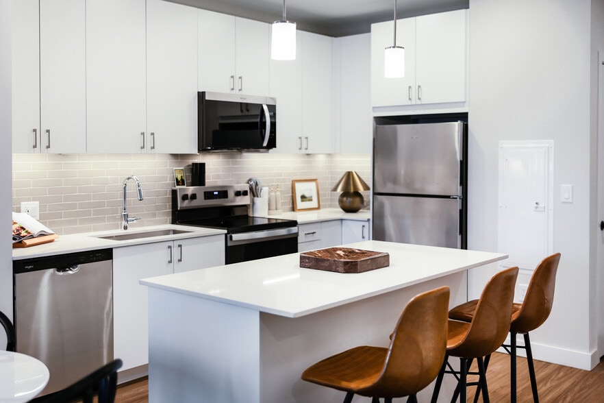Upgrade Collection I kitchen with stainless steel appliances, white cabinetry, grey tile backsplash, under-cabinet lighting, white quartz countertops, and hard surface flooring - Avalon Quincy Adams