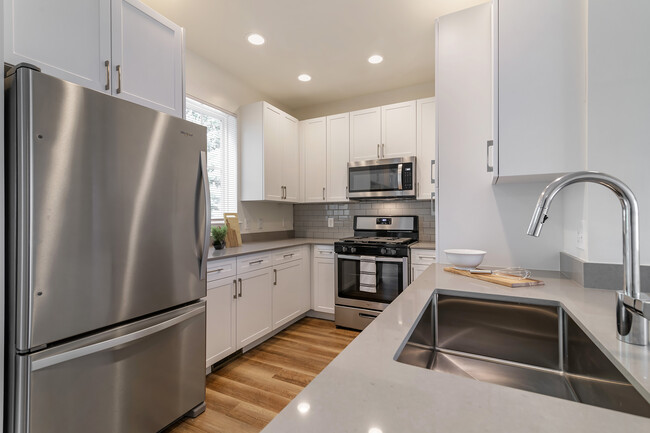 Renovated Package II kitchen with white cabinetry, grey quartz countertops, grey subway tile backsplash, stainless steel appliances, and hard surface flooring - Avalon Northborough