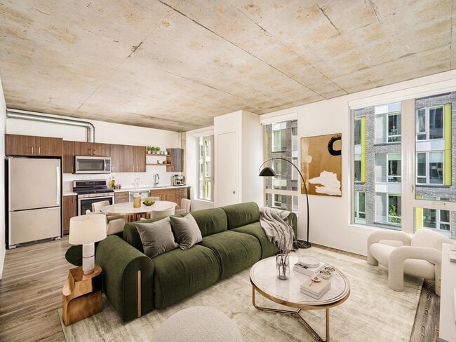 An open apartment home with concrete ceilings, expansive windows, and a streamlined kitchen, offering flexible living space filled with natural light. - Modera Pearl