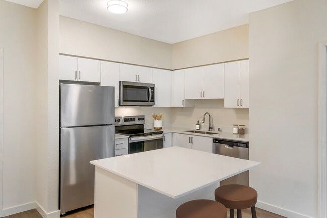 Renovated Package I kitchen with stainless steel appliances, white quartz countertops, white cabinetry, and hard surface flooring - Avalon ParcSquare