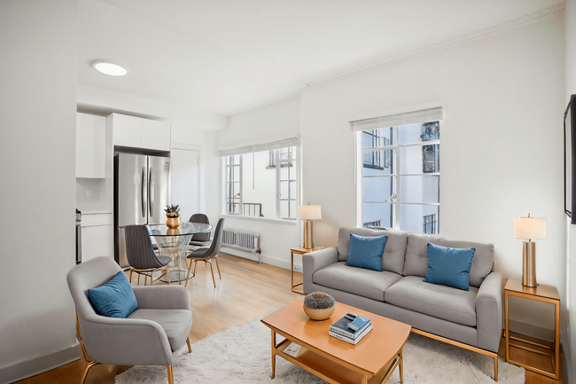 Living room with large window allowing natural light to flood the space, features a sofa. coffee table, dining table with chairs and a refrigerator - 2363 Le Conte Avenue