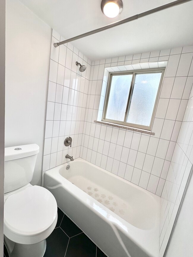 Bright, modern bathroom featuring sleek white tiles, a pristine bathtub, and contemporary fixtures. - Columbine Plaza
