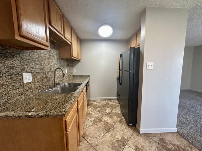 Modern kitchen with granite countertops, wood cabinetry, and sleek appliances leading to a cozy living area. - Boardwalk Apartments