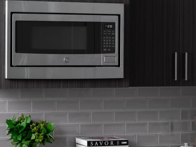 Elegant kitchen featuring sleek GE stainless steel microwave, modern slow close dark wood cabinetry, and stylish subway tile backsplash. - 30 Court Street Apartments