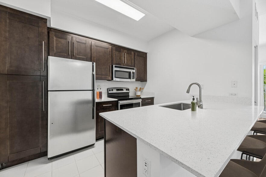 Renovated Package II kitchen with stainless steel appliances, tile backsplash, quartz countertops, and oak cabinetry (in most homes) - Avalon Coconut Creek
