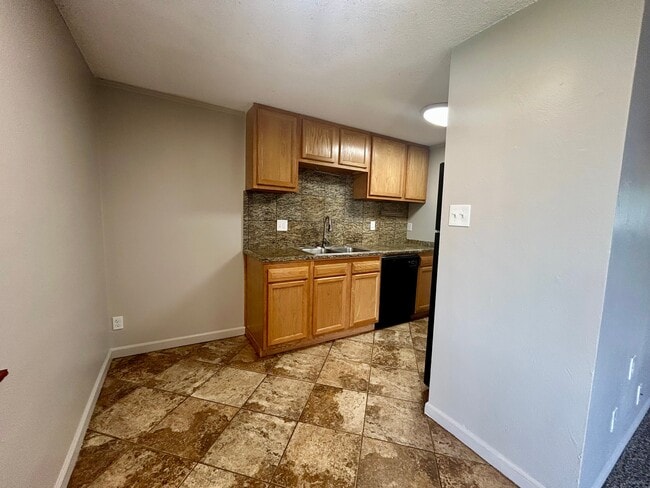 Charming kitchen with elegant wood cabinetry, granite backsplash, and tiled floor, offering a warm and inviting atmosphere. - Boardwalk Apartments