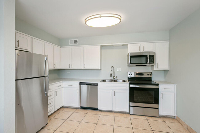 Modern kitchen with stainless steel appliances, white cabinetry, and sleek tile flooring. - LaRonja Apartments