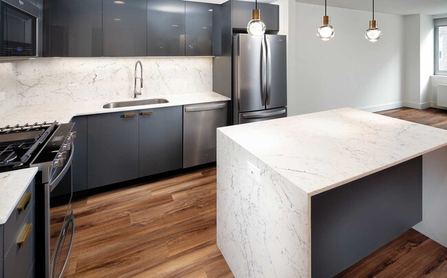 Signature Collection kitchen with pendant lighting, quartz stone countertop with waterfall edge, cabinetry with matte and high gloss finish, and SMART stainless steel appliances - Avalon Bowery Place