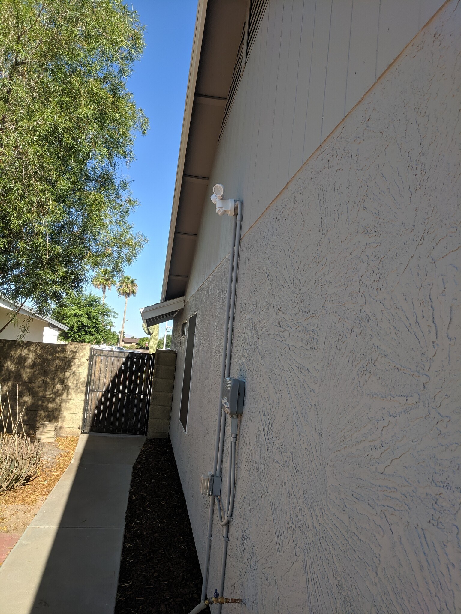 South wall of home and gate to front yard. Security light and irrigation controller in view. - 14101 N 78th Dr