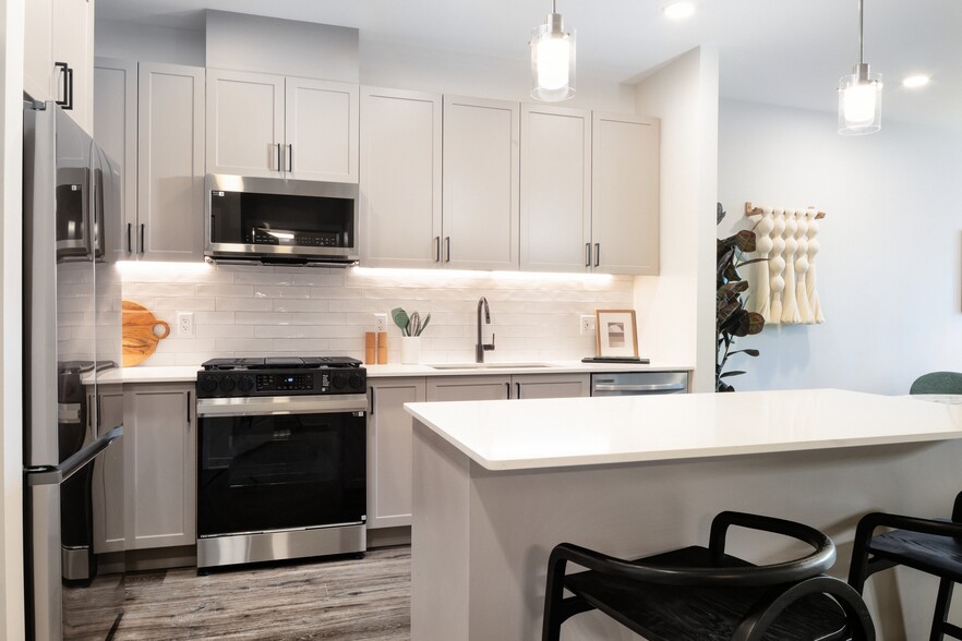 Modern kitchen with grey cabinetry, white tile backsplash, white quartz countertops, stainless steel appliances, and pendant lighting - Avalon Princeton on Harrison