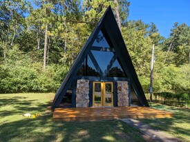 A modern A-frame cabin with a stone entryway, large glass windows, and a peaceful wooded backdrop. - 2406 Crockett Cir