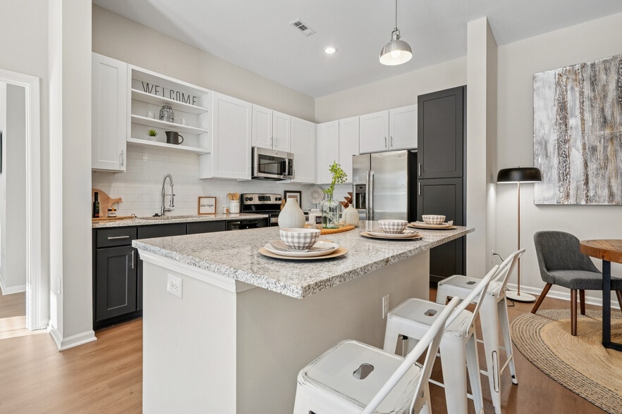 Kitchen with white and dark cabinetry, speckled granite countertops, white subway tile backsplash, stainless steel appliances, and hard surface flooring - Avalon at Palisades