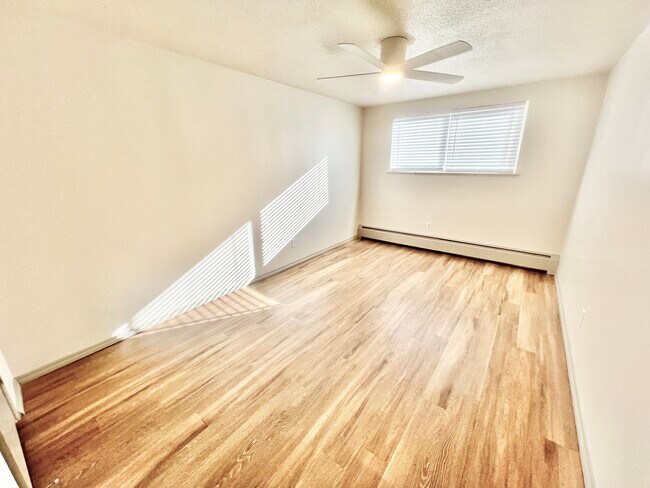 Step into a bright, spacious bedroom with natural light and sleek wooden flooring. - Harmony Apartments