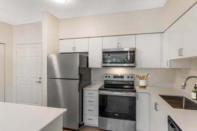 Renovated Package I kitchen with stainless steel appliances, white quartz countertops, white cabinetry, and hard surface flooring - Avalon ParcSquare