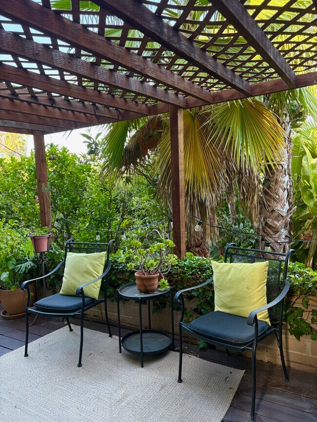Peaceful shaded deck furnished with cushioned wrought-iron chairs and a side table. - 1672 Rotary Dr