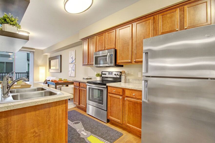 An open kitchen with stainless steel appliances and shelving with a view through to the living area - The Artiste