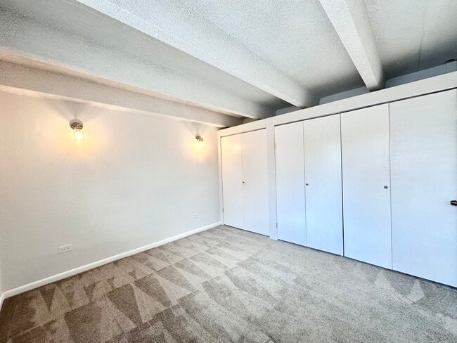 Bright and inviting bedroom with plush carpet, built-in closets, and ambient wall lighting. - Columbine Plaza